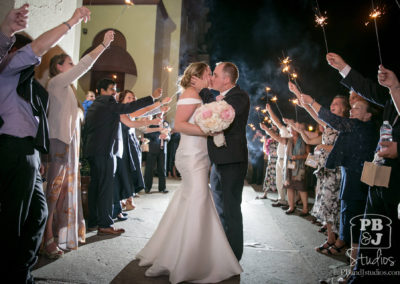 Kate and Steven kissing outside venue with guests holding sparklers